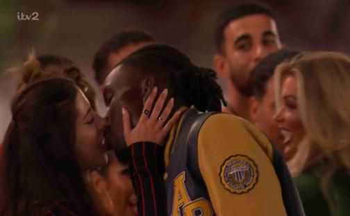 Couple kissing, surrounded by other people.