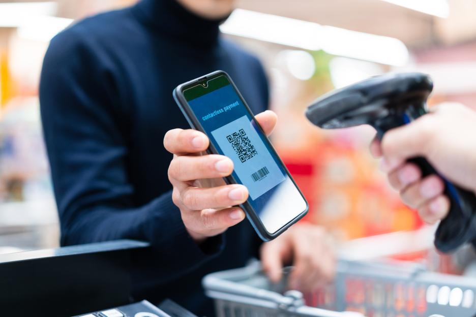 Man using contactless payment app on smartphone at supermarket checkout.