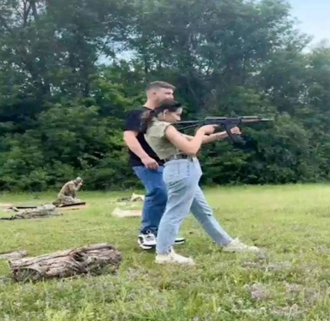 A woman holding an assault rifle, with a man assisting her.