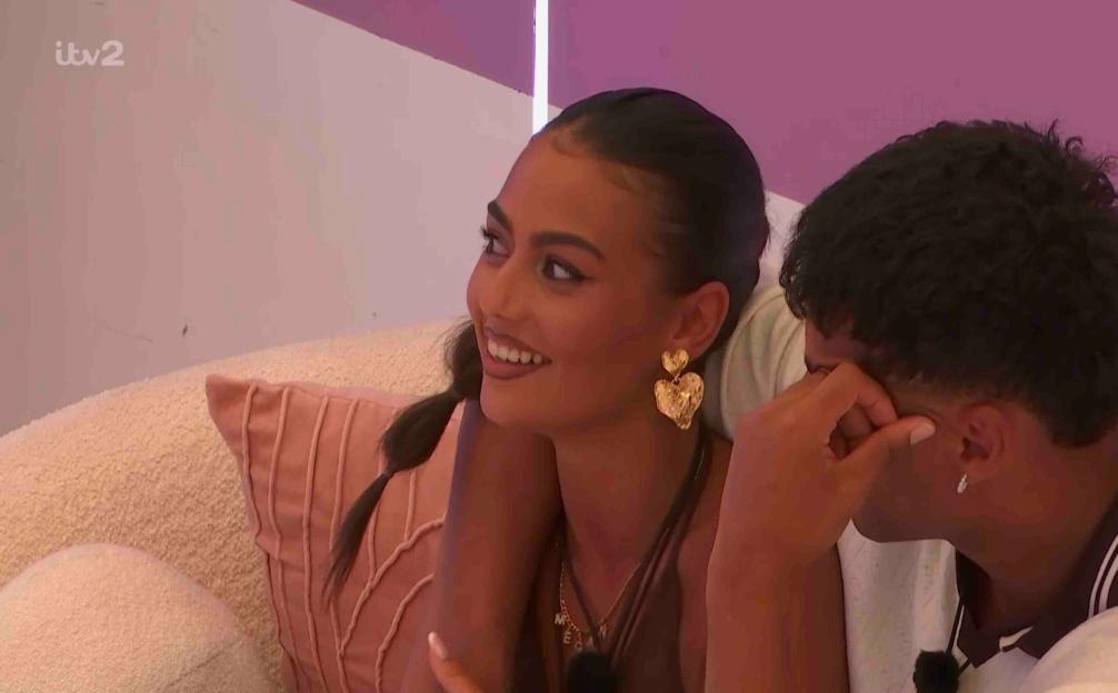 Screenshot of a man and woman from Love Island. The woman is smiling and the man is upset.
