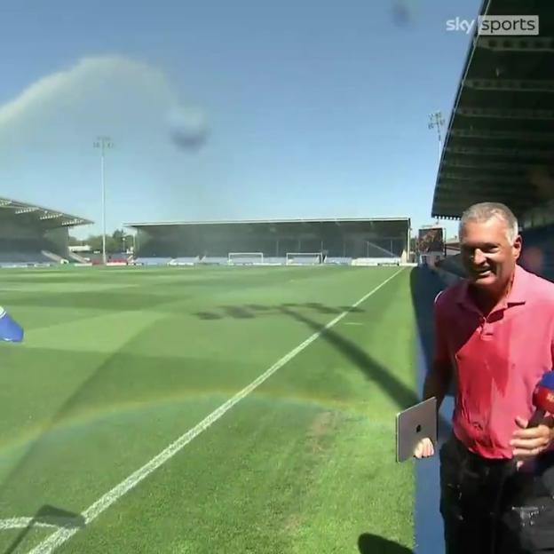 Sky Sports reporter gets soaked by sprinklers during a live broadcast at a soccer stadium.