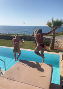 Two women jumping into a pool overlooking the ocean.
