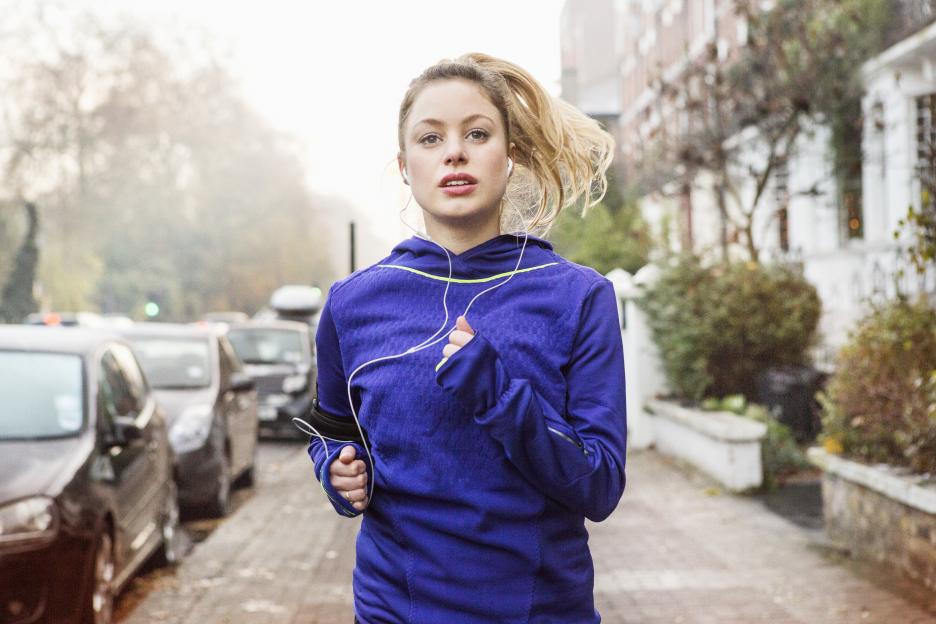 Woman jogging down a city street while wearing headphones.