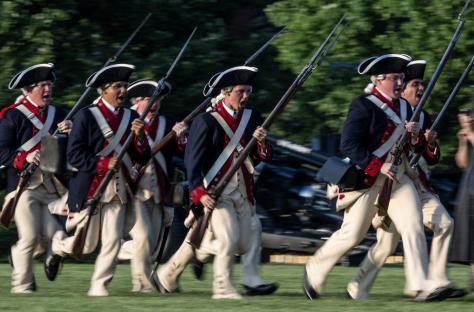 Soldiers in Revolutionary War-era uniforms charging during a US Army Twilight Tattoo event.
