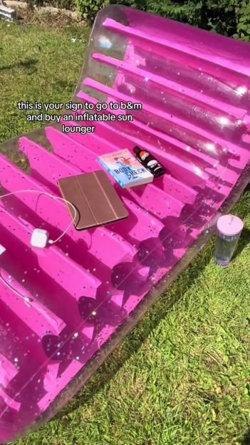 Pink inflatable sun lounger with tablet, book, and drink on it.