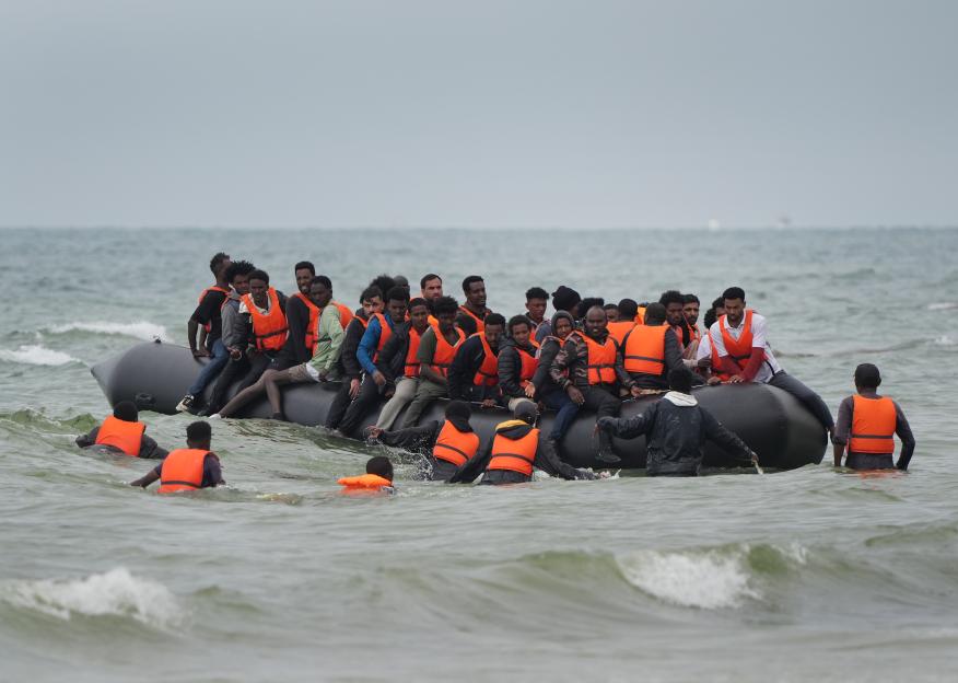 Migrants scramble aboard a small boat in the ocean.