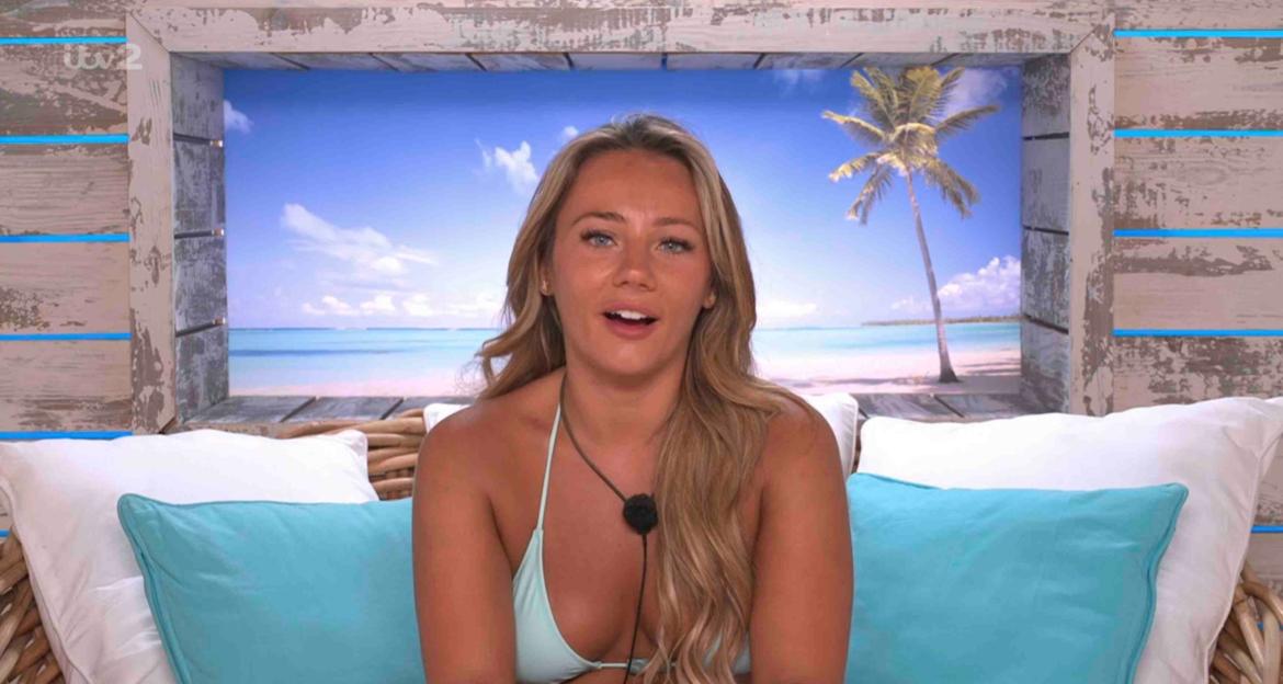 Woman in a light teal bikini sitting on a bed in a beach setting.