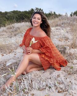 Kelly Brook smiling on a beach, holding a flower.