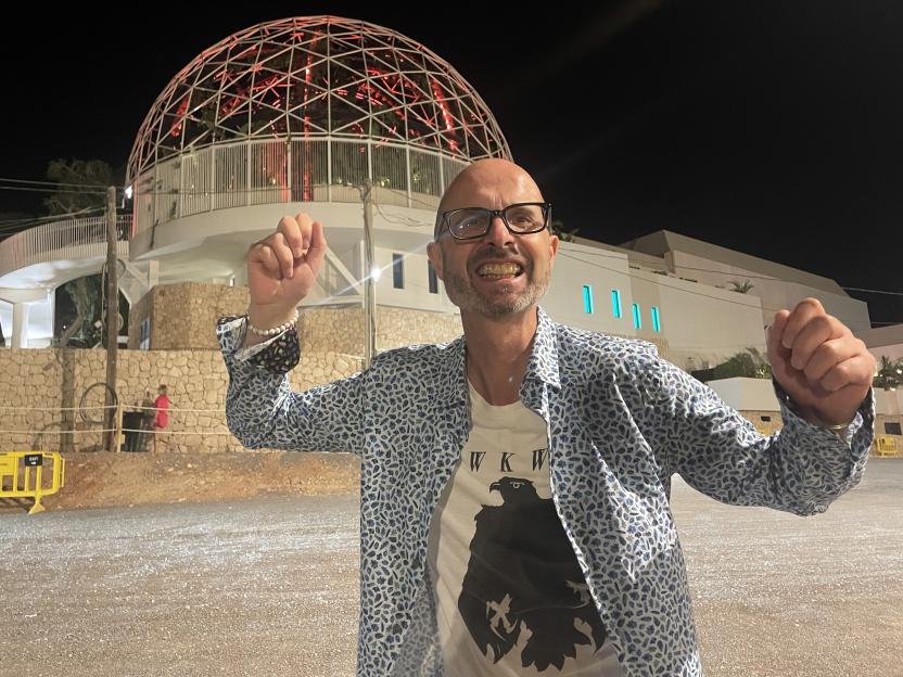 Man in patterned shirt and glasses posing in front of illuminated geodesic dome at night.