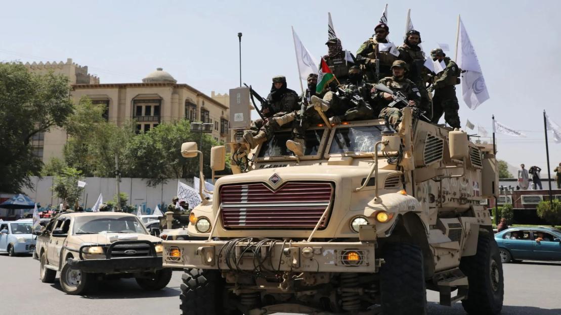 Armed fighters riding on a military vehicle in a city street.