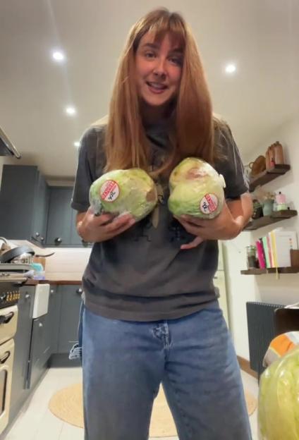 Woman holding two heads of lettuce in a kitchen.