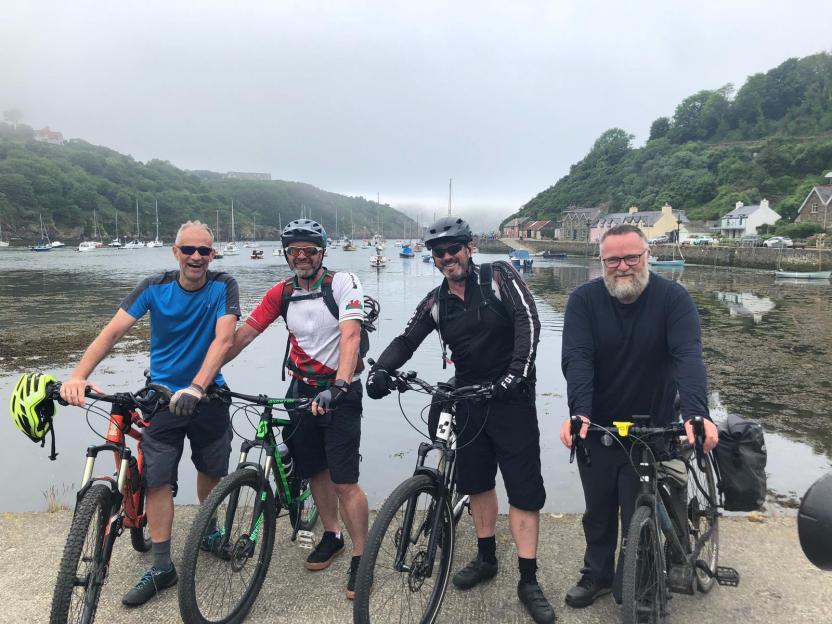 Four cyclists with their bikes in front of a harbor.
