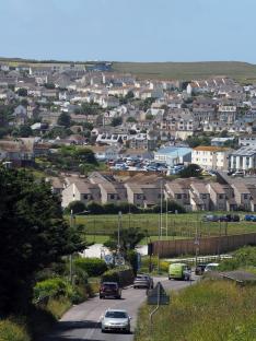 Photo of a coastal town with many houses and cars, and a road leading to it.
