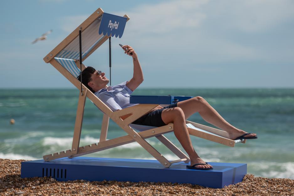 Person using a PayPal branded deckchair on the beach, using their phone.