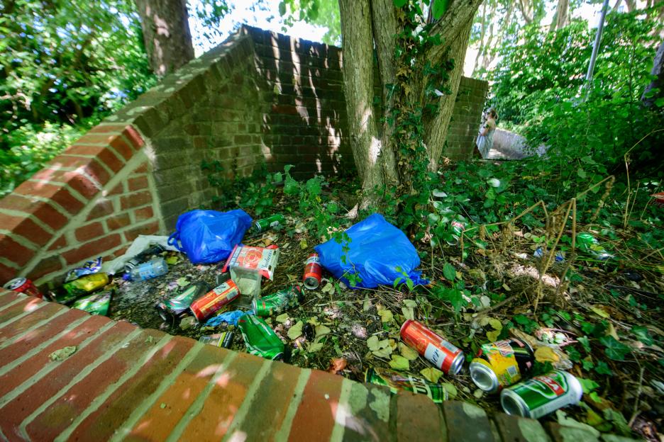 Litter and discarded cans near a brick wall and tree.