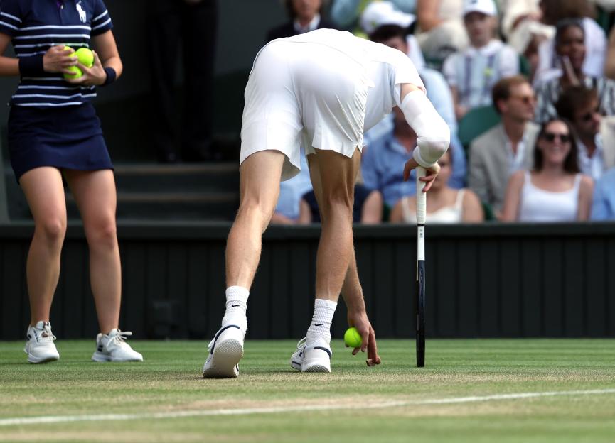 Jannik Sinner picks up a cork during a Wimbledon tennis match.