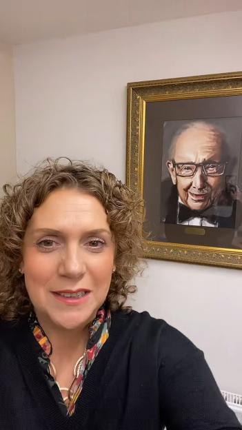 Hannah Ingram-Moore in a video, standing in front of a portrait of Captain Tom.