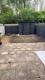 A dark shed in a garden with bare earth and paving stones.