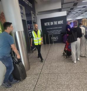Photo of people in an airport with luggage, near a closed M&S Food store.