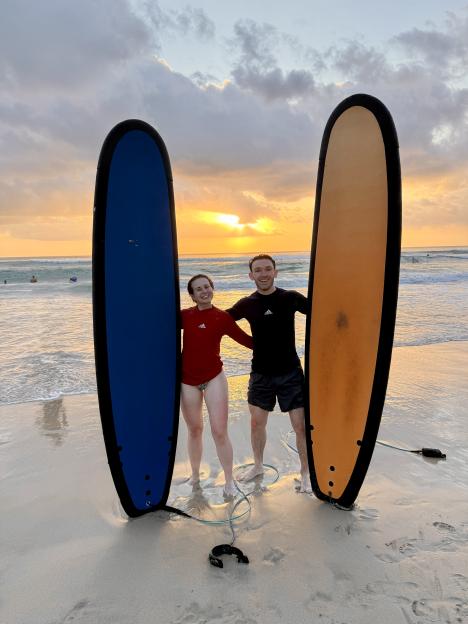 Couple holding surfboards at sunset on Bali beach.