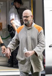 Paul Lewis, handcuffed, in custody.