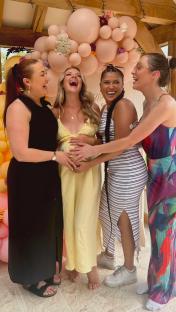 Four women at a baby shower, holding the pregnant woman's belly.