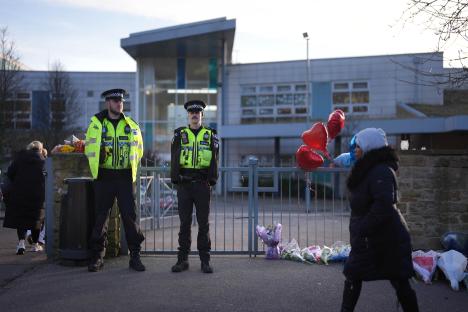 Police officers stand guard outside a school, where floral tributes have been left.
