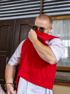 A handcuffed man in a red vest covering his face.