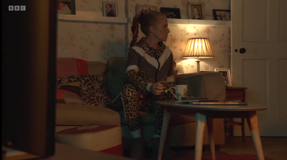 Woman in leopard-print tracksuit sits on sofa in living room.