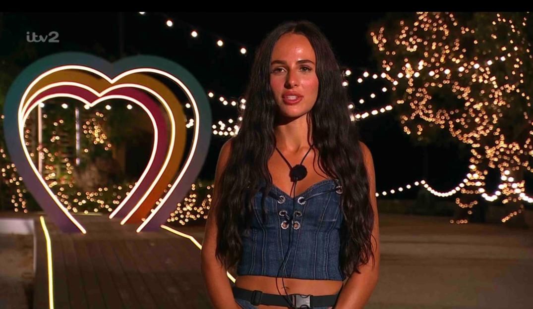 A woman in a denim top stands in front of a heart-shaped light display.