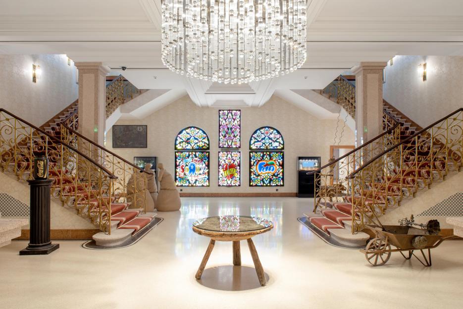 Lobby with two staircases, stained-glass windows, and a low table.