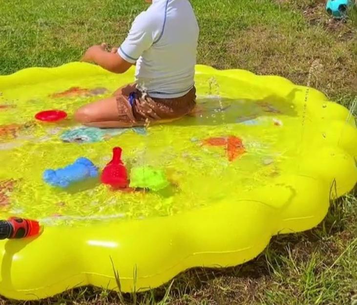 Child playing in a yellow inflatable splash pool in a garden.