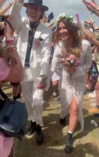 A bride and groom walking through a cheering crowd at a festival.