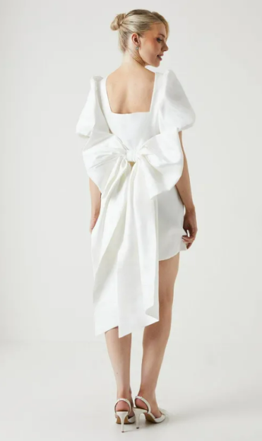 Woman in a white mini dress with a large bow at the back.