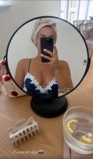 Woman taking a selfie in a mirror, wearing a blue silk pajama top.
