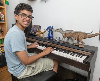 Teenage boy playing keyboard with toys on top.