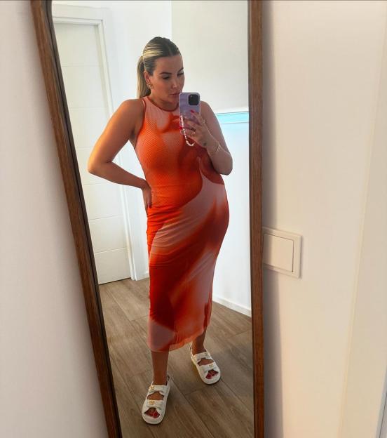 Woman in orange dress taking a selfie in a mirror.