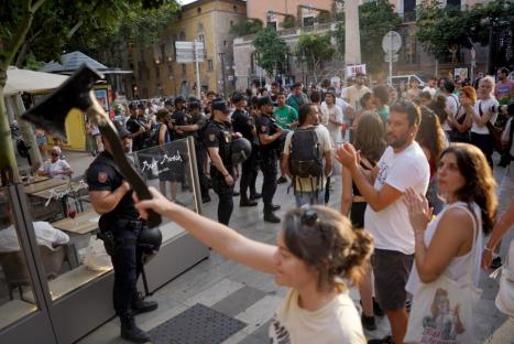 A person holds up an axe in front of a line of police officers during a protest.