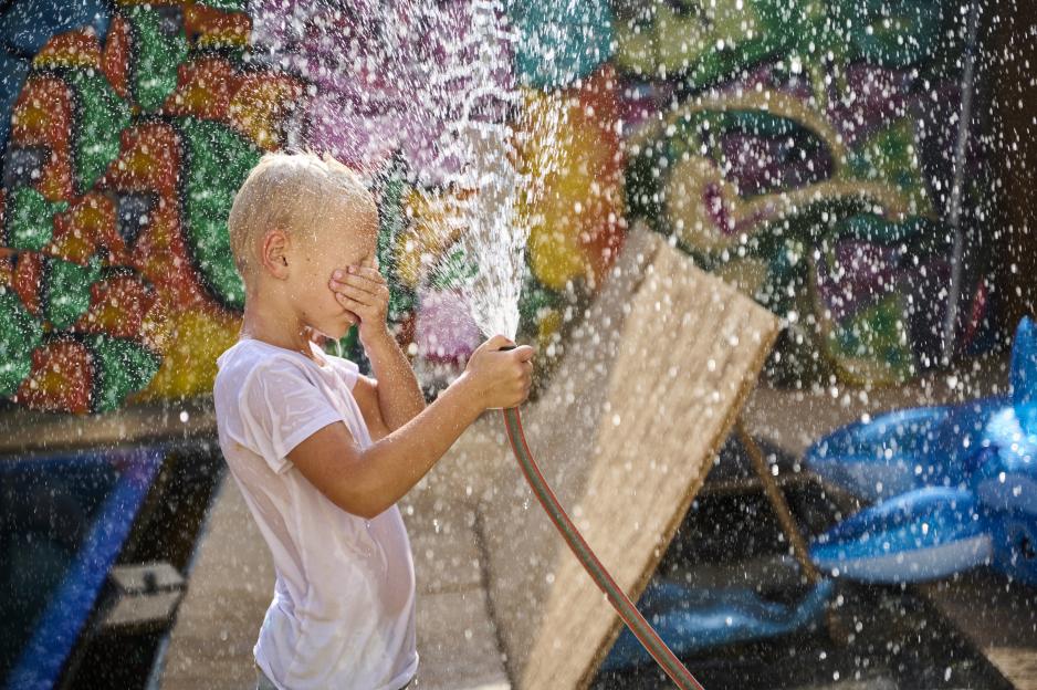 Boy playing with a garden hose, covering his eyes from the spray.