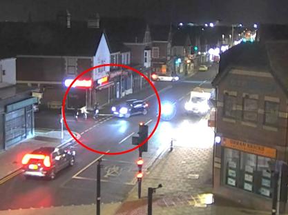 Nighttime security camera footage of a car striking pedestrians in a crosswalk.
