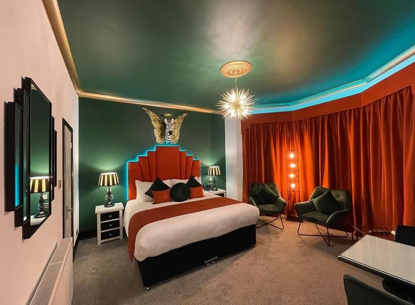 A bedroom with an orange headboard, green walls, and orange curtains.