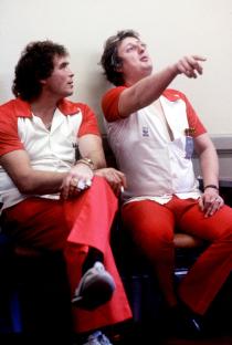 Bobby George watches teammate Eric Bristow demonstrate a dart throw.