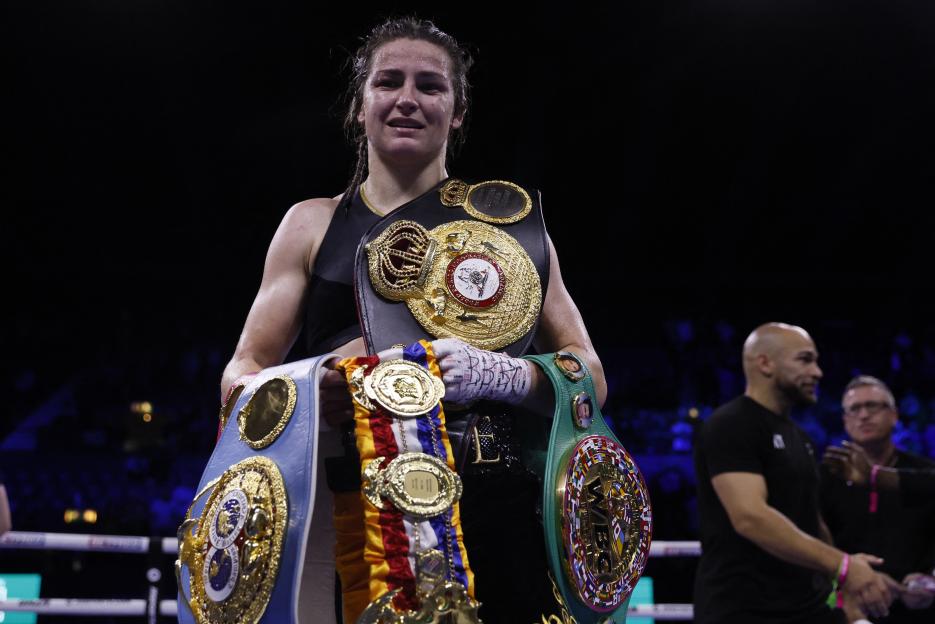 Katie Taylor holding championship belts after a boxing match.