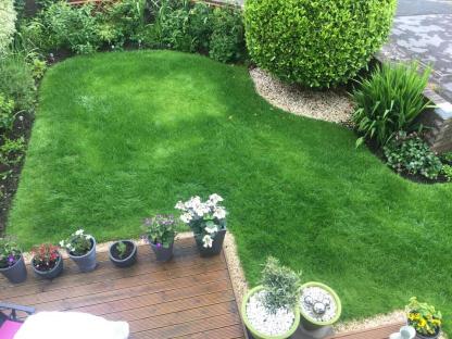 Overhead view of a garden with a green lawn, potted plants, and a wooden deck.