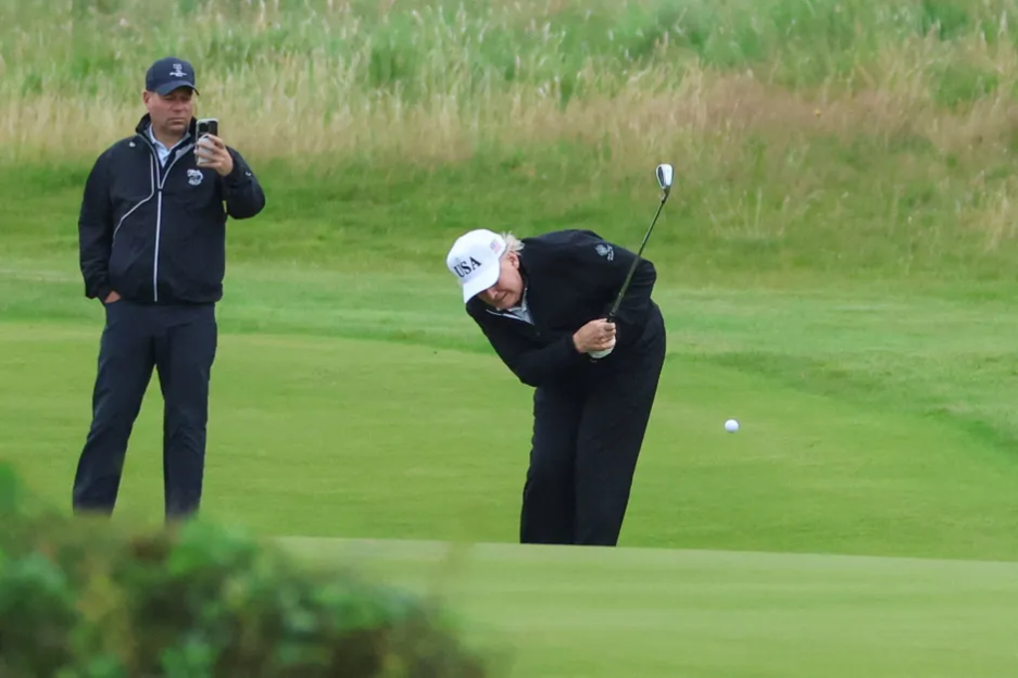 Man golfing while another man watches and films.
