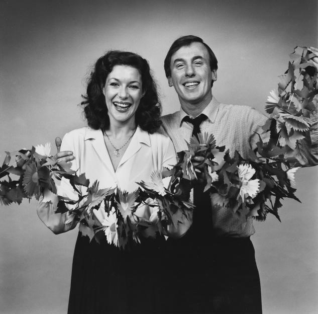 Black and white portrait of Carol Drinkwater and Christopher Timothy holding paper flowers.