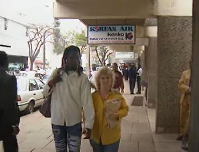 A British woman and a young woman walk down a sidewalk in Kenya, appealing to UK immigration authorities.