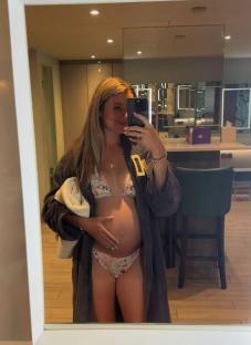 Pregnant woman in a bathrobe taking a selfie in a bathroom mirror.