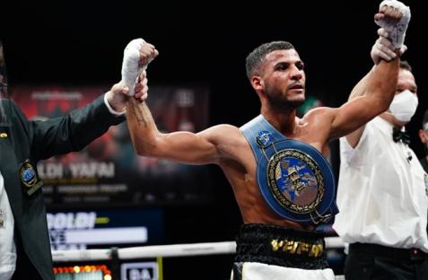 Boxer raising his arms in victory, wearing a championship belt.