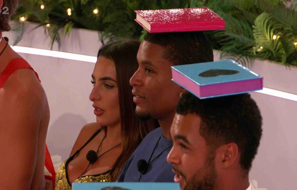 Three Love Island contestants with books balanced on their heads.